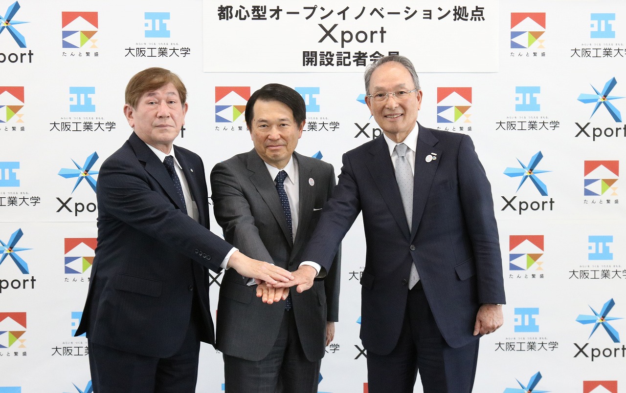 「Xport」の成功を誓い、手を重ねる久禮理事長（右）と西村泰志学長（左）、尾崎会頭