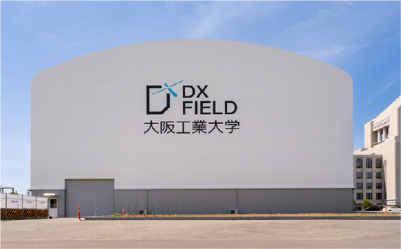 DXフィールドの背面外観写真。真っ白なかまぼこ型の建物の真ん中にDX Fieldのロゴが入っている。