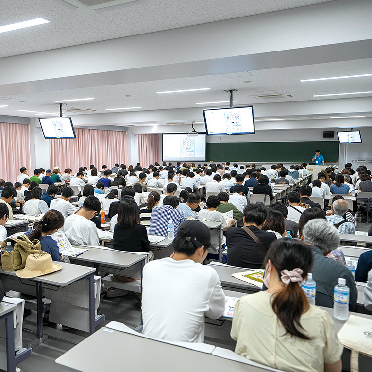 教室いっぱいに机といすが並んでいる。たくさんの生徒が授業を受けている様子。
