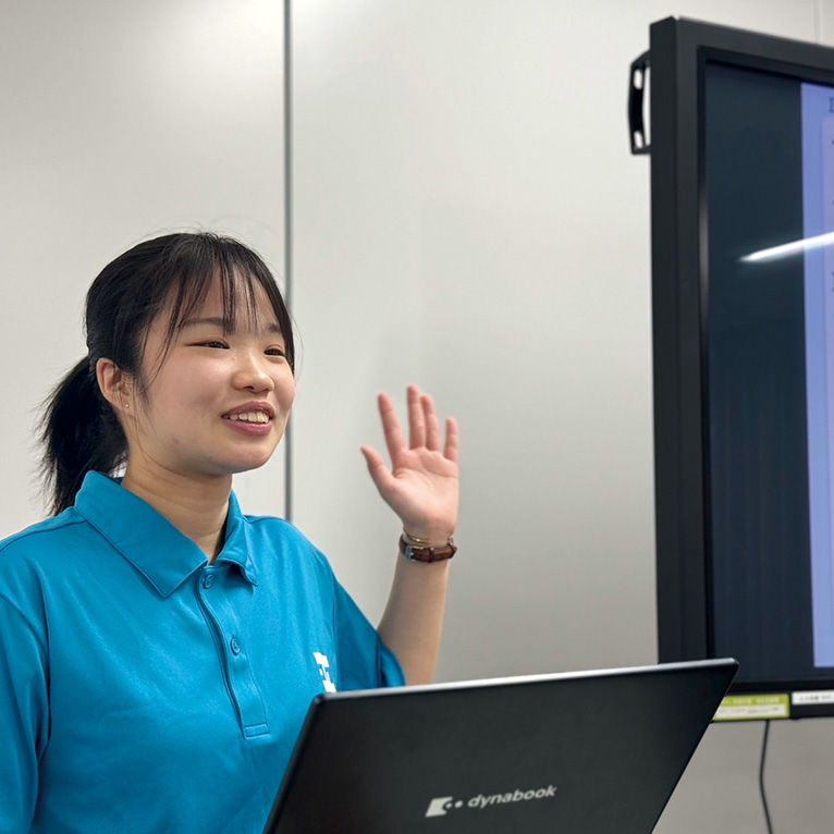 写真：学生スタッフがプロジェクターの隣に立ちプレゼンテーションをしている様子