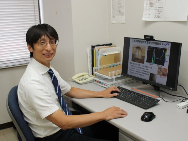 研究資料を表示したパソコンの前に座る鵜飼孝博准教授